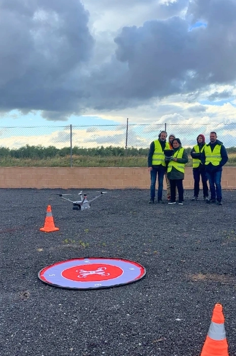 Alumnos con chalecos reflectantes realizando maniobras de despegue y aterrizaje de dron en campo de vuelo con helipuerto portátil y conos de seguridad para el curso de Toledrón.